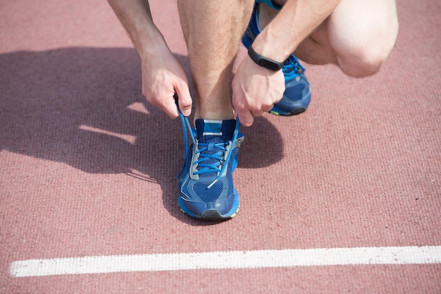 Klaar om te joggen. Handen die schoenveters binden sneaker atletiekbaan achtergrond. Handen van sportman met stappenteller die schoenveters koppelt sportieve sneaker. Running apparatuur concept. Schoenveters strak strikken.