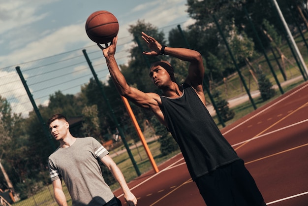 Klaar om te schieten. Twee jonge mannen in sportkleding die basketbal spelen terwijl ze buiten zijn