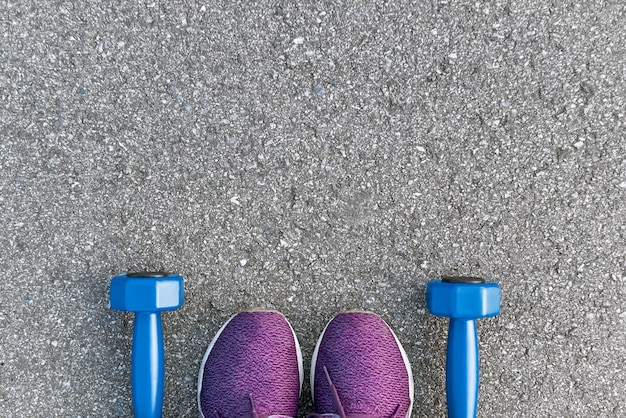 Klaar om te trainen. Bijgesneden foto van dumpbells en paarse sneakers op asfalt achtergrond. Sportmotivatie