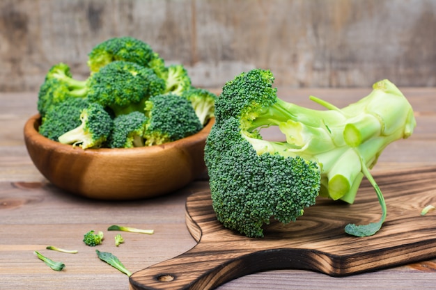 Klaar om verse ongekookte broccoli te eten op een snijplank en verdeeld in bloeiwijzen in een houten bord achter op een houten tafel.