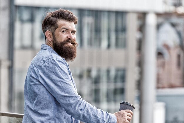 Klaar voor nieuwe dag. Guy bebaarde hipster genieten van alleen koffie. Dagelijkse rituelen. Ochtend koffie concept. Cafeïne energie lading. Persoonlijke efficiëntie. Man drinken meeneem koffie buitenshuis stedelijke achtergrond.