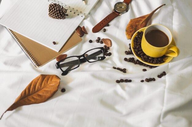 Kladblok brief kopje koffie en een boek met een deken op een witte textiel in bed.