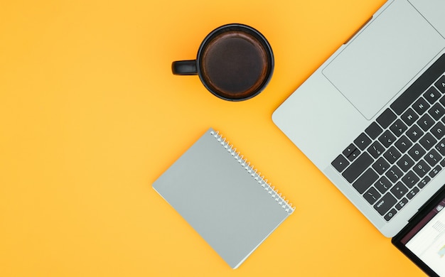 Kladblok, een kopje koffie en een laptop zijn geïsoleerd op een oranje oppervlak en een plek voor de tekst. Copyspace