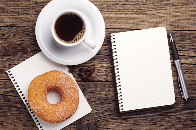 Kladblok en kopje koffie met donut geopend