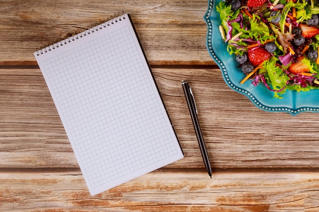 Kladblok en pen met salade op houten tafel