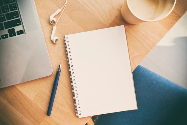 Kladblok, laptop en koptelefoon op houten bureau