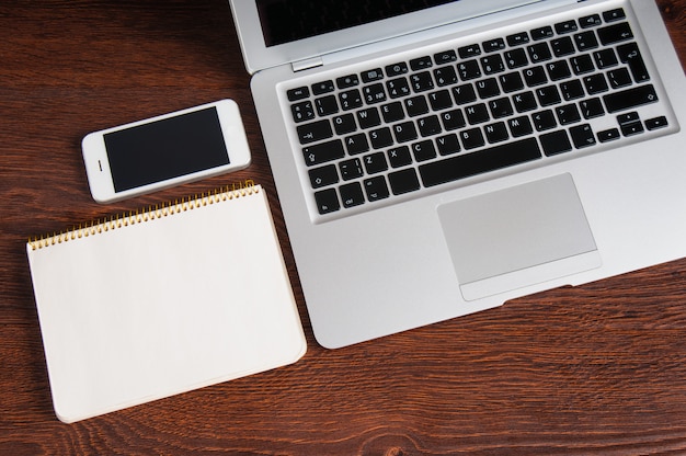 Kladblok, laptop en mobiele telefoon op houten tafel