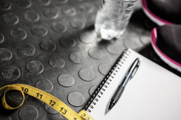 Kladblok, meetlint, schoenen en fles in de sportschool