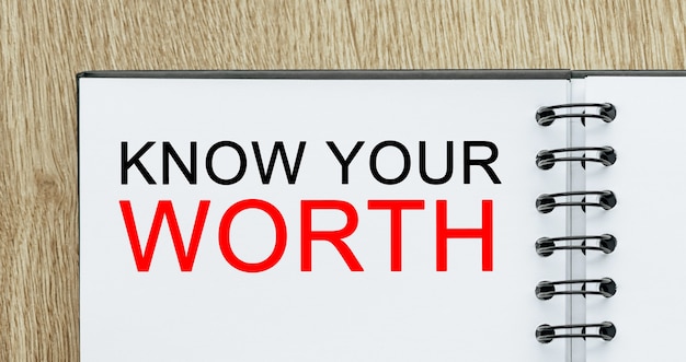 Kladblok met tekst KNOW YOUR WORTH op houten bureau. Zakelijk en financieel concept