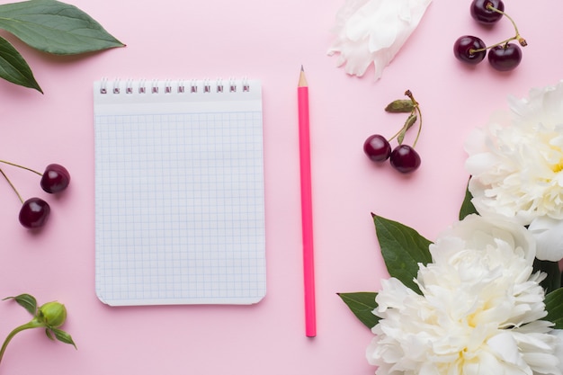 Kladblok voor tekst witte bloemen pioen cherry bessen op pastel roze oppervlak