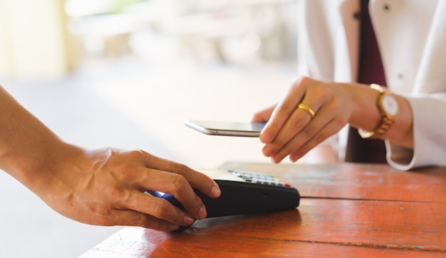 klant hand met smartphone voor het betalen van rekening met behulp van betaalautomaat aan tafel