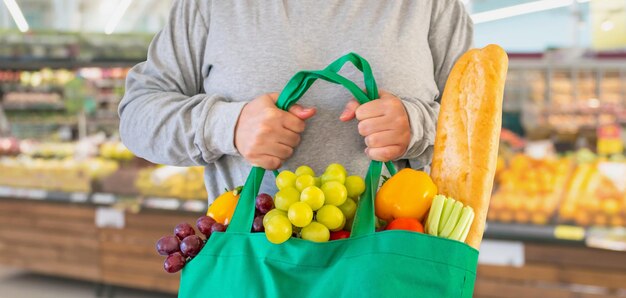 Klant houdt boodschappentas met fruit en groente over supermarktachtergrond