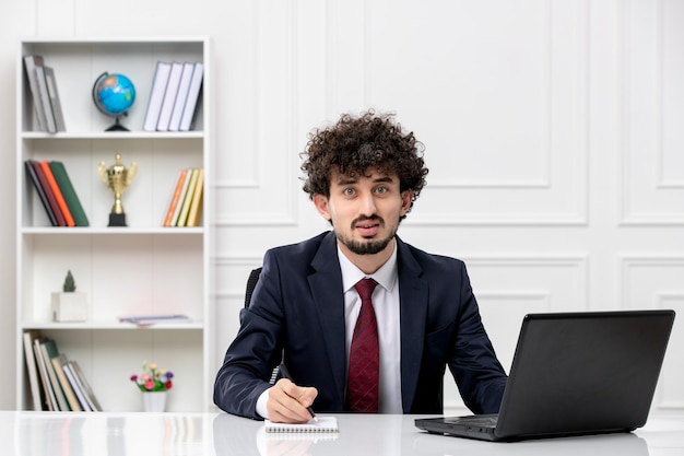 Klantenservice gekrulde brunette jonge man in kantoorpak met laptop die notities opschrijft