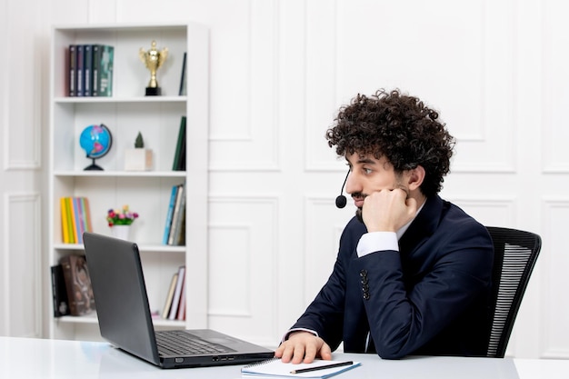 Klantenservice knappe krullende man in kantoorpak met computer en headset denken