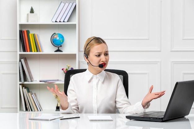 Klantenservice mooi blond meisje in wit overhemd met laptop en headset geïrriteerd en geïrriteerd