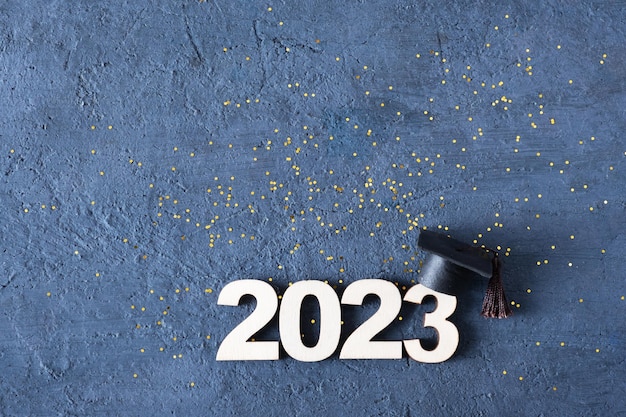 Klasse van 2023 concept Houten nummer 2023 met afgestudeerde hoed op donkere betonnen achtergrond met klatergoud bovenaanzicht