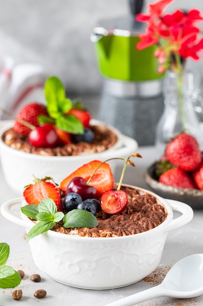 Klassiek Italiaans dessert Tiramisu versierd met aardbeien, kersen en munt op een witte achtergrond.