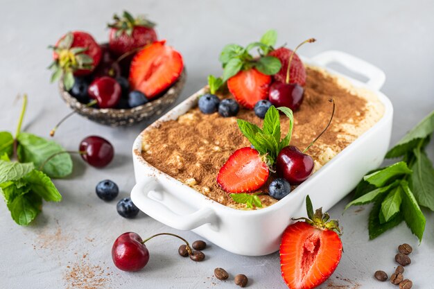 Klassiek Italiaans dessert Tiramisu versierd met aardbeien, kersen en munt op een witte achtergrond.