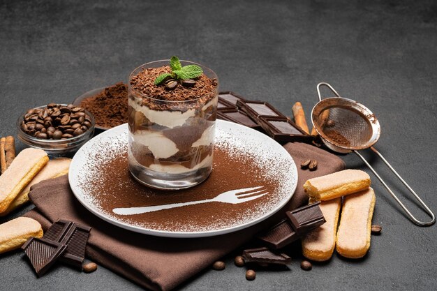 Klassiek tiramisu-dessert in een glas en kopje koffie op donkere betonnen achtergrond