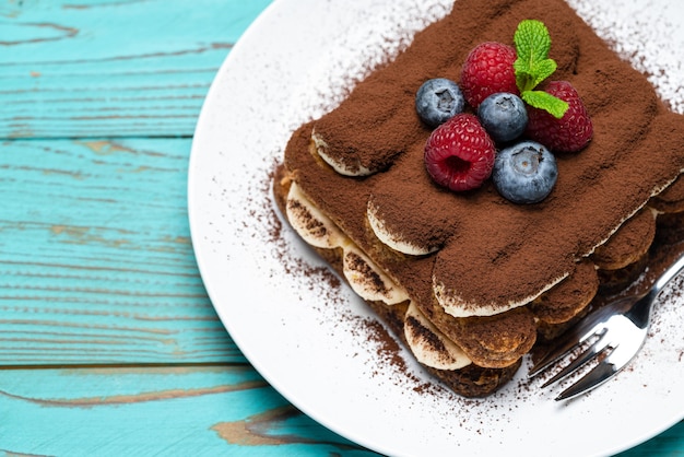 Klassiek tiramisudessert met frambozen en bosbessen op blauwe houten tafel