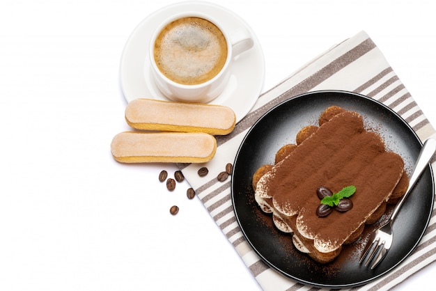 Klassiek tiramisudessert op ceramische plaat, savoiardikoekjes en kop van koffie die op witte oppervlakte met het knippen van weg wordt geïsoleerd