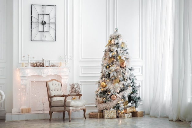 Klassiek wit kerstbinnenland met versierde boom. Open haard met grijze stoel, klokken aan de muur en cadeautjes onder de boom