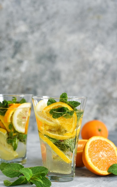 Klassiek zomers koud drankje - limonade met sinaasappel, citroen en munt op een betonnen ondergrond.