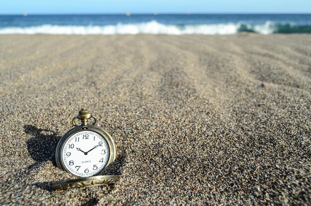 Klassieke analoge klok in het zand op het strand bij de oceaan