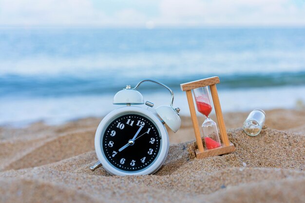 Foto klassieke analoge klokken en een boodschap of brief in een fles met een zandklok op het tropische strand