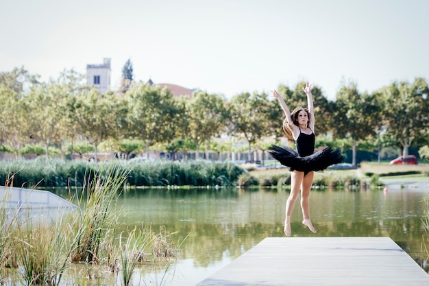 Klassieke ballerina die op een zonnige dag op een voetgangersbrug van een stedelijk meer springt