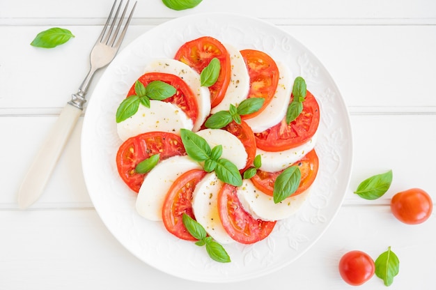 Klassieke caprese salade met mozzarella kaas, tomaten en basilicum op een wit bord