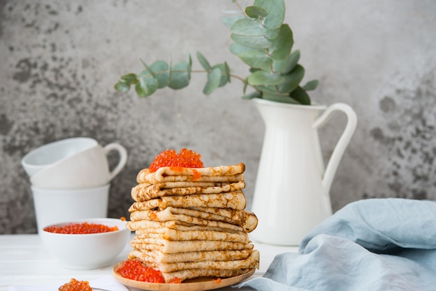 Klassieke dunne kant pannenkoeken op een houten plaat met rode kaviaar op een lichte achtergrond. Een traditioneel gerecht voor Vastenavond.