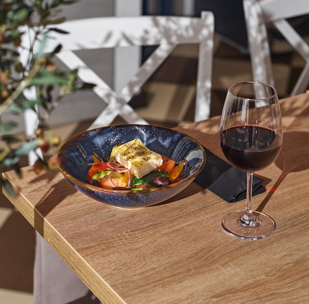 Klassieke Griekse salade van tomaten, komkommers en kaas Plaat van salade en een glas wijn op een tafel in een restaurant