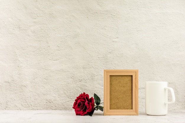 Klassieke houten fotolijst en rode roos met een witte koffiekop.