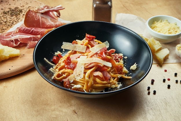 Klassieke, huisgemaakte pasta met rode saus, parmezaan, ham en zongedroogde tomaten in zwarte kom. Traditionele Italiaanse keuken