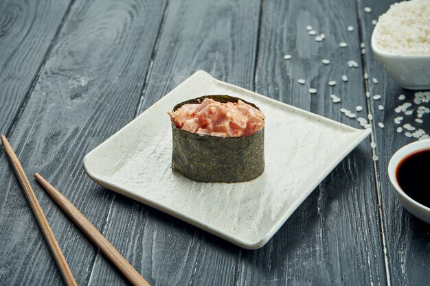 Klassieke Japanse sushi rolt - gunkan met tonijn en kruidige witte saus op een witte ceramische plaat op een zwarte houten achtergrond. Detailopname