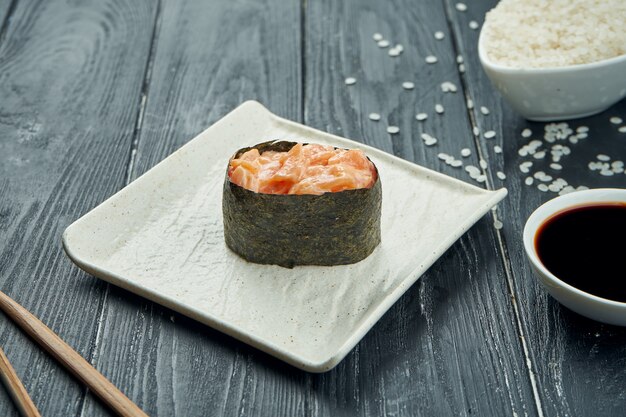 Klassieke Japanse sushi rolt - gunkan met zalm en kruidige witte saus op een witte ceramische plaat op een zwarte houten achtergrond. Detailopname