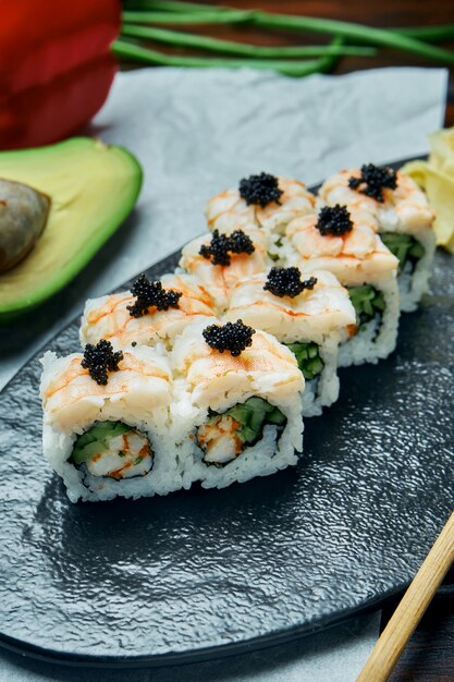 Foto klassieke japanse sushi rolt met garnalen, krab en kaviaar. california roll op een zwarte plaat met stokjes. japanse keuken. gezonde zeevruchten
