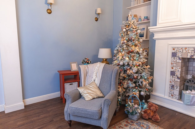 Klassieke kerst ingerichte binnenkamer, nieuwjaarsboom met zilveren versieringen. Moderne blauwe klassieke stijl interieur appartement met open haard en fauteuil. Kerstavond thuis.