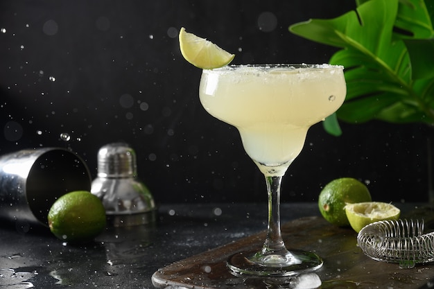 Klassieke margarita-cocktail met limoensap en ijsblokje op zwarte achtergrond met splash