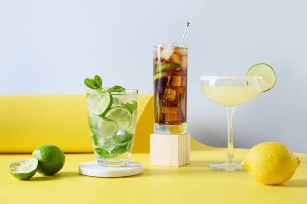 Klassieke mojito, cuba libre, margarita cocktail met limoen en citroen op moderne kleur gele achtergrond. Drie zomerse frisheidsdranken voor een feestelijk feest. Vakantie aperitief.