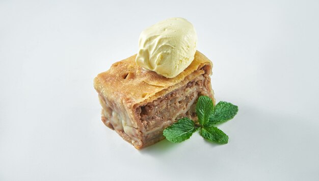 Klassieke Oostenrijkse bladerdeegstrudel met appel en vanille-ijs geïsoleerd op een witte tafel. Close-up, selectieve aandacht