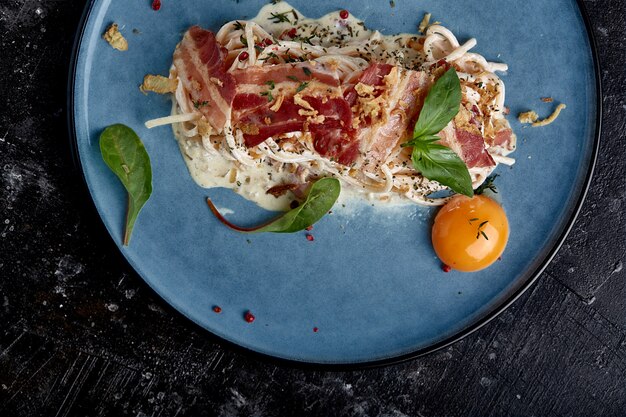 Klassieke pasta carbonara met dooier op een bord. Pasta opgemaakt op een blauw bord op een donkere. Concept van de Italiaanse keuken, mooie gerechten, close-up.