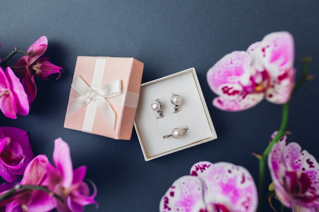 Klassieke retro stijlvolle sieraden. Zilveren ring oorbellen met parels in geschenkverpakking met paarse orchidee. Modieuze accessoires