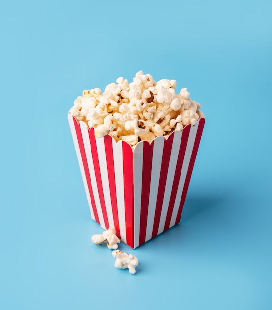 Klassieke rode en witte doos popcorn die op blauw wordt geïsoleerd