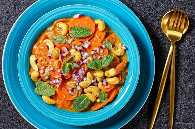 Foto klassieke wortelcurry met cashewnoten en rozijnen in een blauwe kom op een betonnen tafel, horizontale weergave van bovenaf, plat gelegd, close-up, indiase keuken