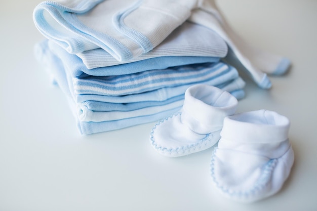 kleding, babytijd, moederschap en objectconcept - close-up van babyslofjes en stapel kleren voor pasgeboren jongen
