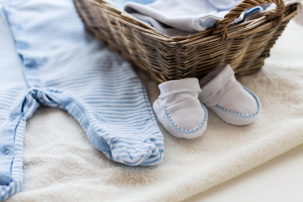 kleding, babytijd, moederschap en objectconcept - close-up van witte babyslofjes met stapel kleren en handdoek voor pasgeboren jongen in mand op tafel