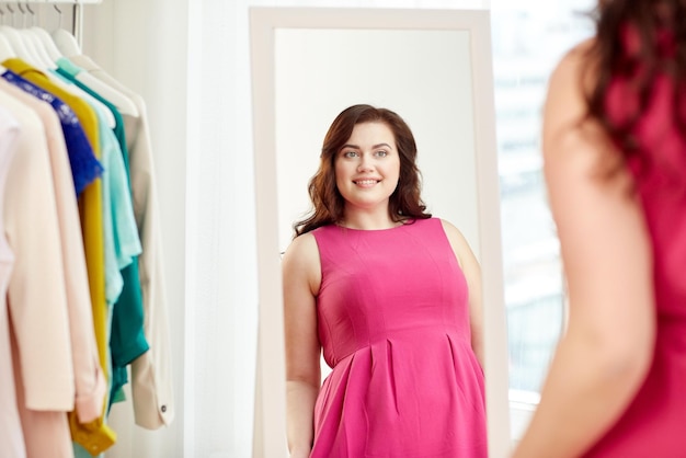 kleding, garderobe, mode, stijl en mensenconcept - gelukkige plus size vrouw die zich voordeed in de spiegel thuis