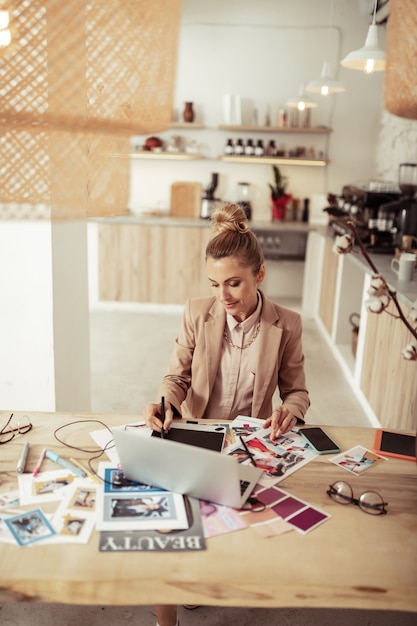 Kleding maken. Glimlachende modeontwerper tekenen schetsen zittend aan de tafel met haar laptop.